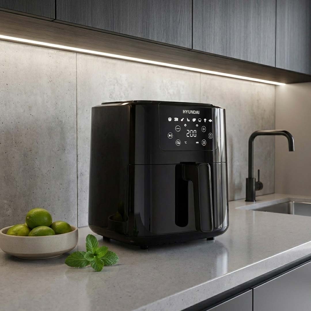 Black Hyundai air fryer on a kitchen counter with a bowl of limes and a sink in the background.