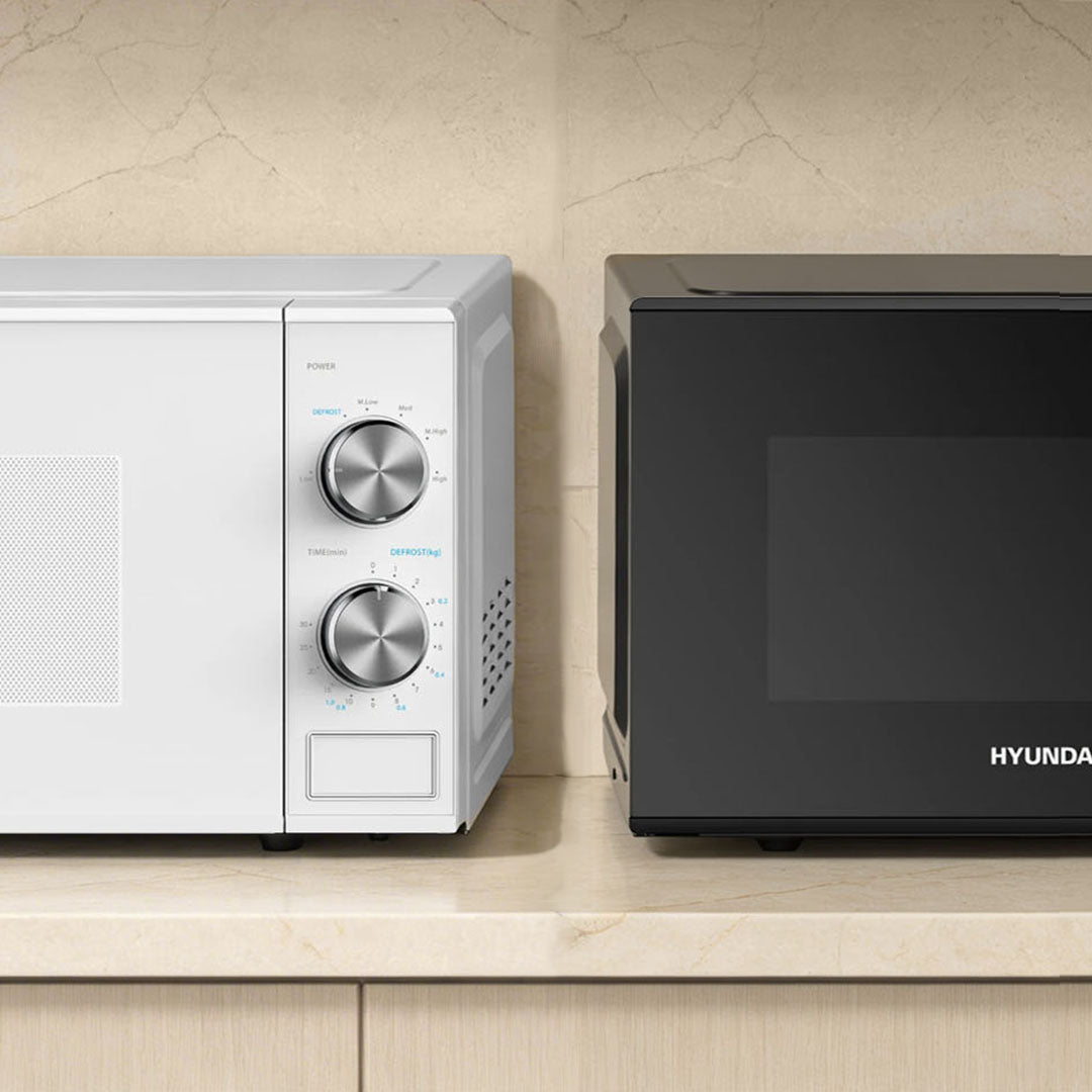 Two microwaves, one white with silver knobs and one black with 'HYUNDAI' branding, on a beige countertop.
